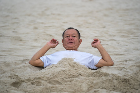 Danang, Vietnam - June 15, 2020: Vietnames man taking a bath of beach sand for therapy near sea water in the morning on the city Danang, Vietnam. Local people relax on the beachのeditorial素材