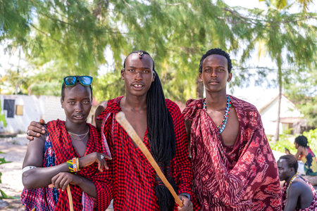 Zanzibar, Tanzania - December 12, 2019: African three men masai dressed in traditional clothes standing near the ocean on the sand beach of Zanzibar island, Tanzania, East Africa, close upのeditorial素材
