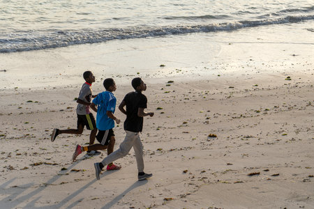Zanzibar, Tanzania - December 12, 2019: Three young African guys run in the morning on a tropical beach near the sea of Zanzibar island, Tanzania, East Africaのeditorial素材