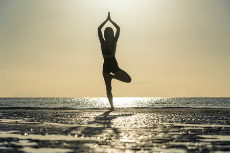 Silhouette of woman standing at yoga pose on the tropical beach during sunset. Caucasian girl practicing yoga near sea waterの写真素材