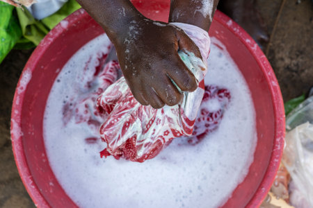 African female hands washing clothes in basin on a street near home of Zanzibar island, Tanzania, East Africa. Wash stain of dirty clothing by hand with detergent. Close upの写真素材