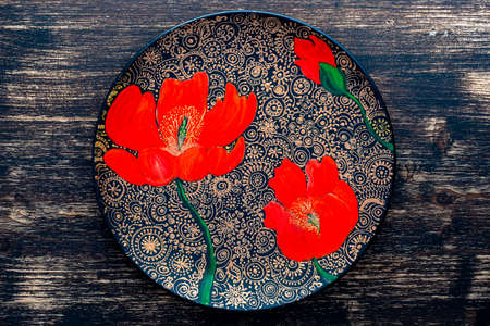 Decorative ceramic plate with red poppies, painted plate on wooden background, close up, top view....