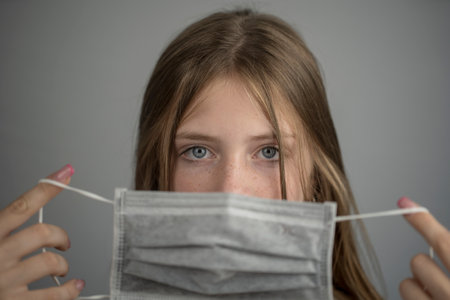Studio portrait of young girl wearing a face mask, close up, on gray background. Flu epidemic, dust allergy, protection against virus. City air pollution concept. Copy spaceの写真素材