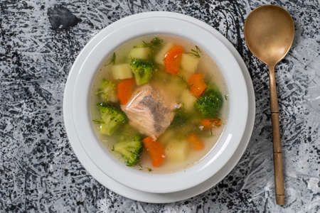 Fresh salmon fish soup with carrots, potatoes and onions in a white plate, close up. Tasty dinner consists of a fish soup with salmon. Top viewの写真素材