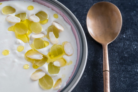 Traditional Spanish dish, cold soup ajo blanco or ajoblanco from garlic, almonds, white wine vinegar, olive oil and green grapes in a bowl with a spoon, close upの写真素材