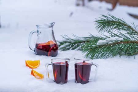 Glass with mulled red wine on a bed of snow and white background. Mulled wine or punch with slice of orange and anise star and cinnamon, close up. Christmas beverage.の写真素材