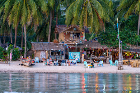 KOH PHANGAN, THAILAND - MAY 18, 2019: Beach bar, coconut palm trees and sea water during sunset at tropical island Koh Phangan, Thailandのeditorial素材