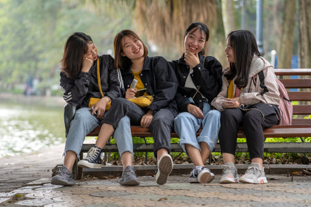 Hanoi, Vietnam - march 01, 2020: Happy young Vietnamese girls are sitting on a bench next to a lake in the center of the old city of Hanoi, Vietnamのeditorial素材