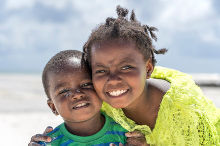 Zanzibar, Tanzania - December 12, 2019: Young happy African girl and boy near sea water on the tropical beach in island of Zanzibar, Tanzania, east Africa, close upのeditorial素材