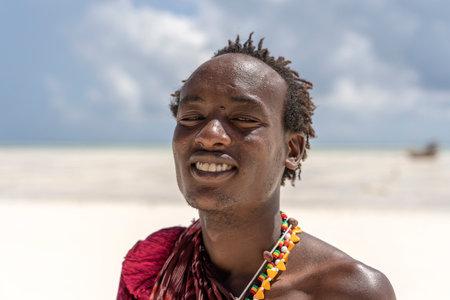 Zanzibar, Tanzania - December 12, 2019: African man masai dressed in traditional clothes standing near the ocean on the beach of Zanzibar island, Tanzania, East Africa, close upのeditorial素材