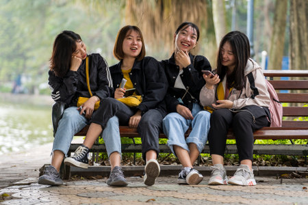 Hanoi, Vietnam - march 01, 2020: Happy young Vietnamese girls are sitting on a bench next to a lake in the center of the old city of Hanoi, Vietnamのeditorial素材