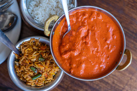Navratan saffron biryani with fresh vegetables, spices and basmati rice in a metal pot and pieces of chicken in red curry sauce on wooden background, top view, close up. Indian cuisineの写真素材