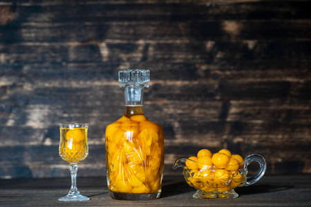 Homemade tincture of yellow cherry plum in a crystal bottle and a wine crystal glass on wooden background, Ukraine, close up. Berry alcoholic drinks conceptの写真素材