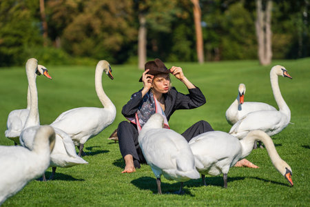 Kyiv, Ukraine - September 10, 2020: Ukrainian girl rest on the green lawn with wild white swans at sunny day in park, close up. Kyiv, Ukraineのeditorial素材