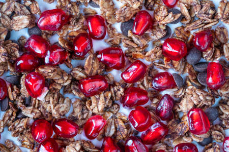 Granola with oatmeal, dried fruit, honey, raisins, chocolate chips, nuts and red pomegranate seeds with yogurt in a black bowl, close up, top view. Healthy breakfast conceptの写真素材