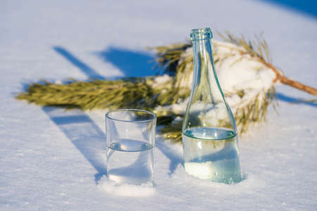 Glass bottle and glass of water on a white snow in winter, close upの写真素材