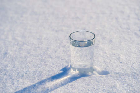 Glass with water on a white snow in winter, close upの写真素材