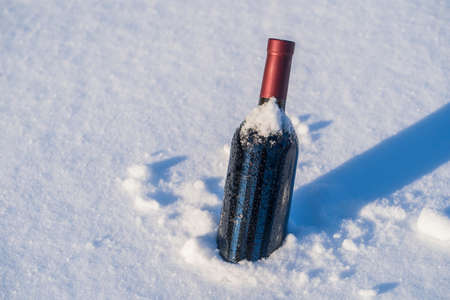 Bottle of red wine on a bed of snow and white background, close upの写真素材