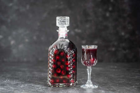 Homemade tincture of red cherry in a glass bottle and a wine crystal glass on gray background, Ukraine, close up. Berry alcoholic drinks conceptの写真素材
