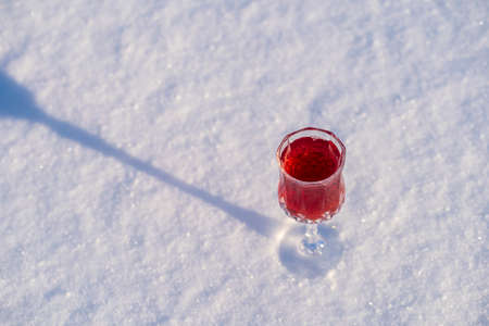 Homemade tincture of red cherry in a wine crystal glass on a snow and white background, Ukraine,...