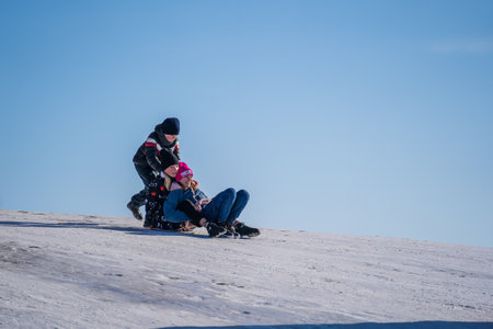Shepetivka, Ukraine - january 21, 2021: Children sledding with mountain warm winter day. Ukrainian children having fun on snowy small mountain during the winter in Shepetivka, Ukraineのeditorial素材