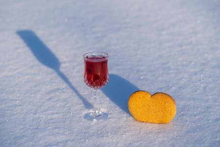 Homemade tincture of red cherry in a wine crystal glass and heart shaped christmas cookies on a white snow in winter, close upの写真素材