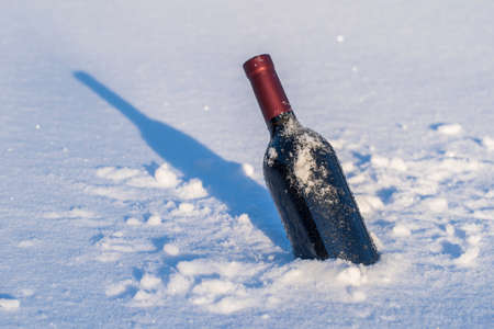 Bottle of red wine on a bed of snow and white background, close upの写真素材