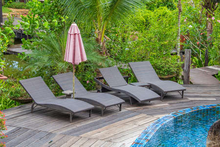 Swimming pool with relaxing beds and sun umbrella in tropical garden near beach in Thailand