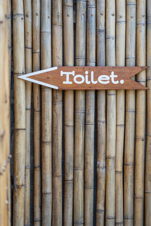 Text toilet on wooden board on bamboo wall on tropical island Koh Phangan, Thailand. Vertical view of simple design handmade wooden sign of toilet give direction to WC. Close up, outdoorsの写真素材
