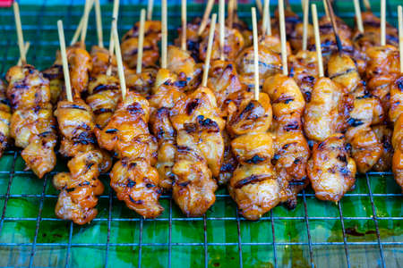 Thai street vendor sells grilled chicken meat at street food market in island Koh Phangan, Thailand. Close up fried chicken buttsの写真素材
