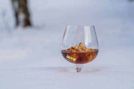 Glass of cognac with ice on a bed of snow and white background, close up. Concept of christmas winter morningの写真素材