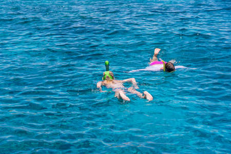 Young girls snorkeling in blue clear waters above coral reef on red sea in Sharm El Sheikh, Egypt. Travel and lifestyle concept. Top view. Two snorkelers swim in turquoise waterの写真素材