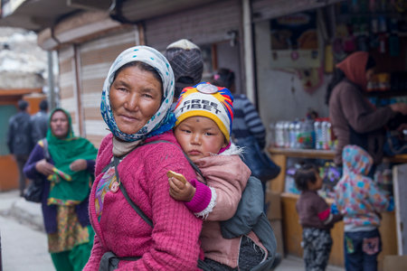 Leh, India - June 21, 2015: Indian poor local woman with the child on the street market in mountain village Leh, Ladakh region, north India, close up. Poverty is a major issue in Indiaのeditorial素材