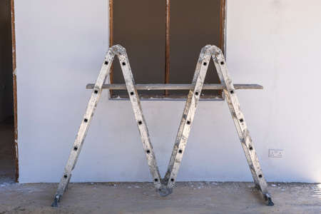 Front view of window frame, ladder and white concrete wall in incomplete house building site, close upの写真素材