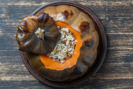 Great pumpkin baked with a filling close-up on a plate, top view, copy space. Stuffed roasted orange pumpkin, whole baked, filled with a tasty mixture of rice, raisins and spicesの写真素材