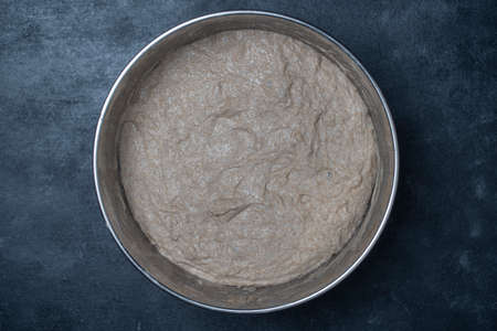 Rye sourdough dough for baking bread in a metal bowl, close up, top view