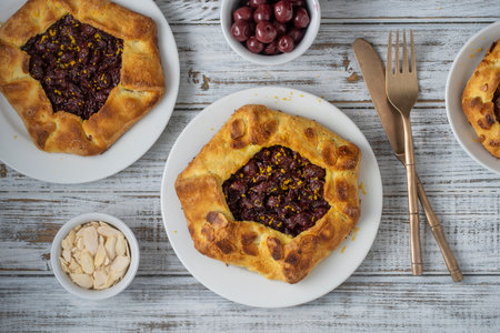 Delicious biscuit with red cherries and almond chips in a white plate on a wooden table, close up, top viewの写真素材