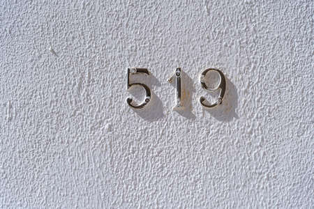 Metal house number 519 on a white stucco wall background, close up