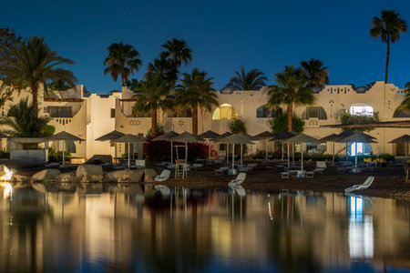 Buildings, sun loungers and parasols are reflected in the calm sea water on the beach at night in the resort town of Sharm El Sheikh, Egyptのeditorial素材