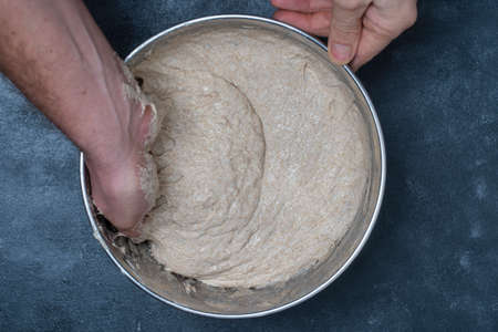 Male baker stretches out yeast-free dough for baking bread with his hands, close up, top view