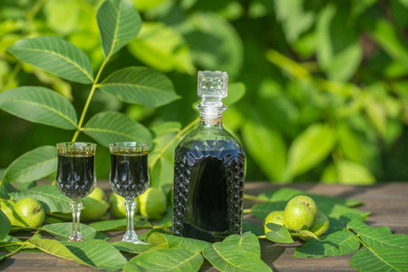 Liqueur from young green walnuts, remedy for stomach ache, close up. Tincture of green walnuts in a glass bottle on a table in the gardenの写真素材