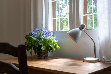 Wooden table with chair, lamp and a bouquet of flowers near the window in modern working area at home, Tanzania, East Africa, close upの写真素材