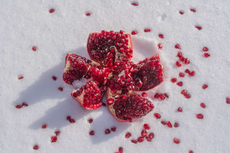 Open pomegranate fruit with red seeds on a white snow in winter, close up. Organic bio fruits