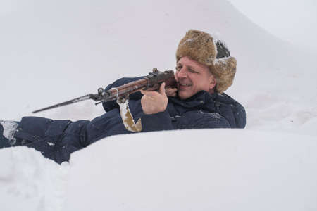 Man and antique Mosin rifle with a bayonet in a snowy trench in winter, Ukraine