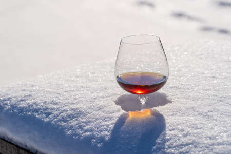 Glass of cognac on a bed of snow and white background, close up. Concept of christmas winter morningの写真素材
