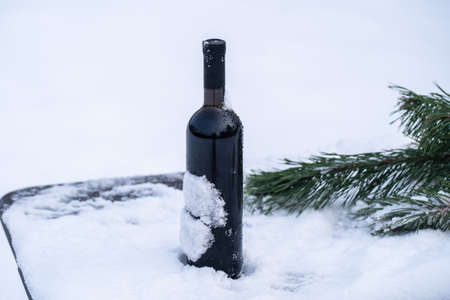 Bottle of red wine on a bed of snow and white background, close upの写真素材