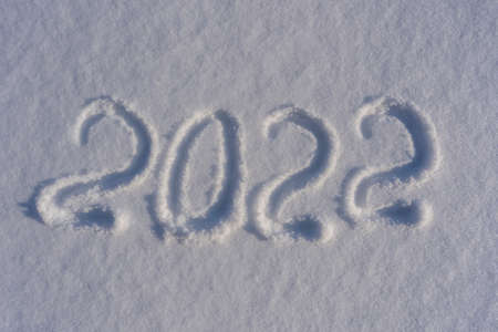 Happy new year 2022 sign text written with numbers from snow on snow surface, symbol of the next year marked against a snowy winter background. Inscription 2022 on a snowdrift in sunlight. New yearの写真素材