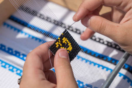 Young girl makes a beaded bracelet with her hands, Ukraine, close up. Elements of embroidery from beads, paintings and handmade by masters of beadsの写真素材