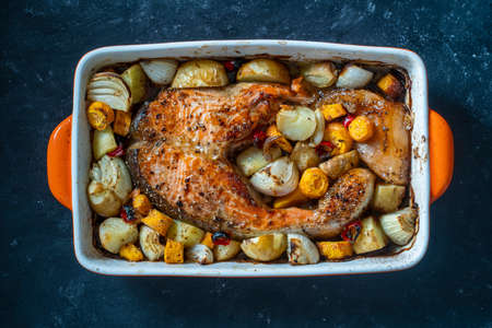 Baked salmon fillet with potatoes, carrots, onions, red peppers and garlic in a ceramic bowl on a...