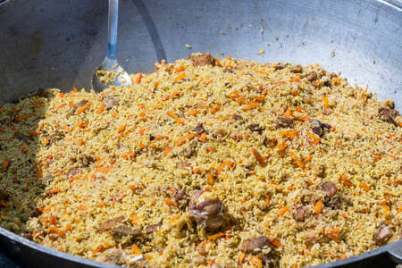 Cooking of traditional pilaf in big cauldron on the street food market in Ukraine, close up